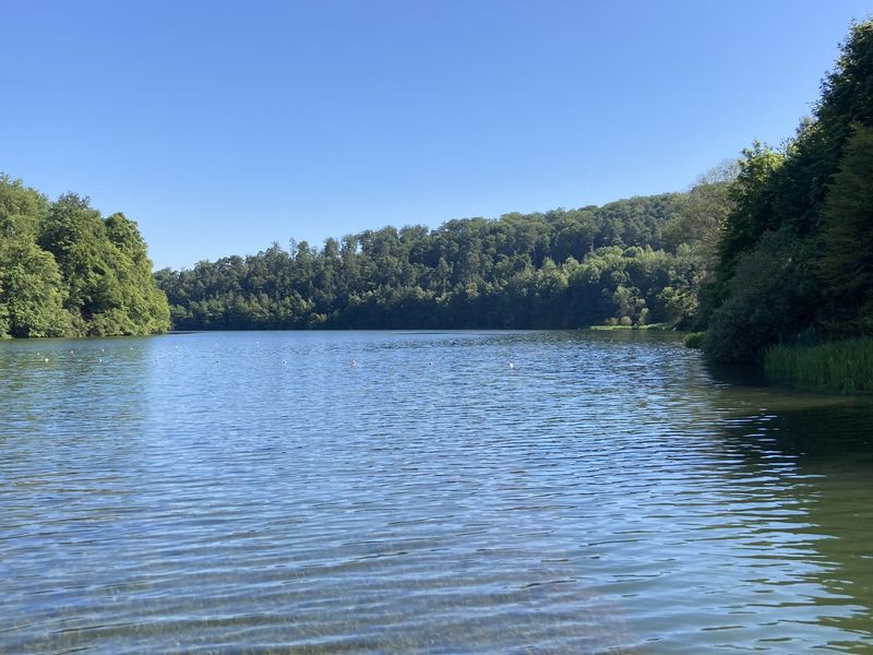 Twistesee mit Bojen im Badebereich, umgeben von bewaldeten Hängen unter blauem Himmel