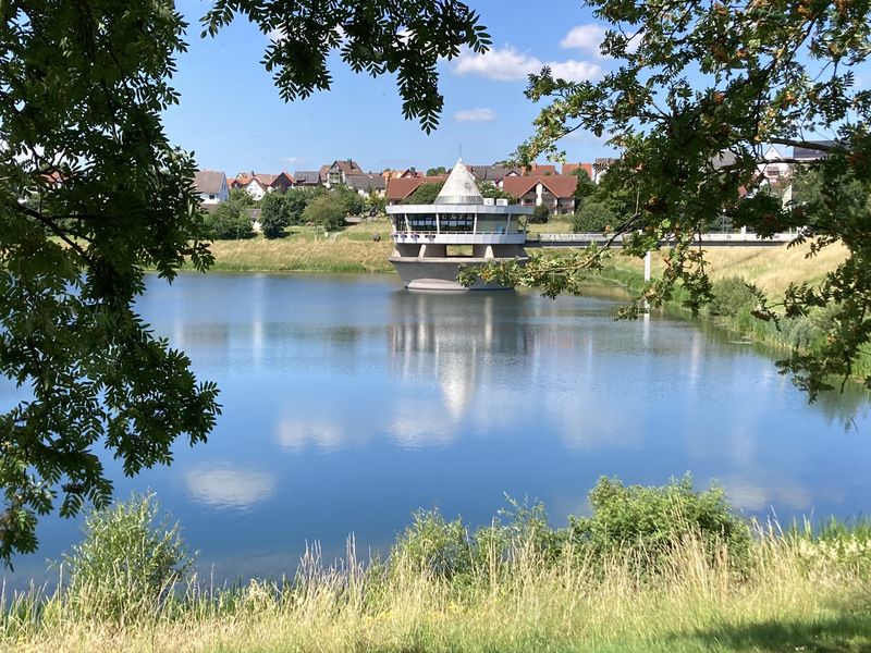 Café-Turm im Wasser, im Hintergrund Häuser des Ortes, gerahmt von Zweigen