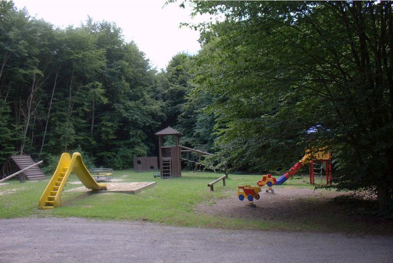 Spielplatz im Wald mit gelber Rutsche, Sandkasten und Klettergerüst